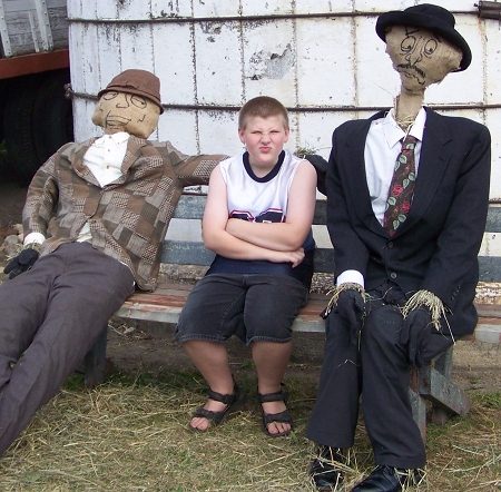 Corbin between two scarecrows on a bench