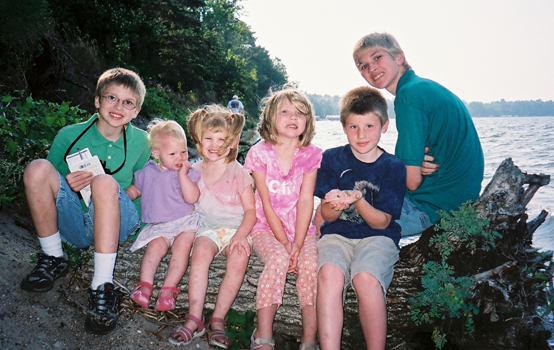 The 6 kids posing on a log overlooking the water.
